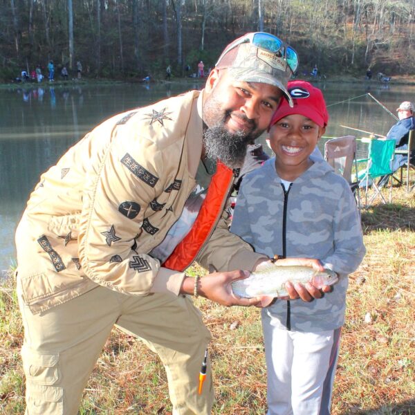 image of father and soon smiling at the camera holding a fish